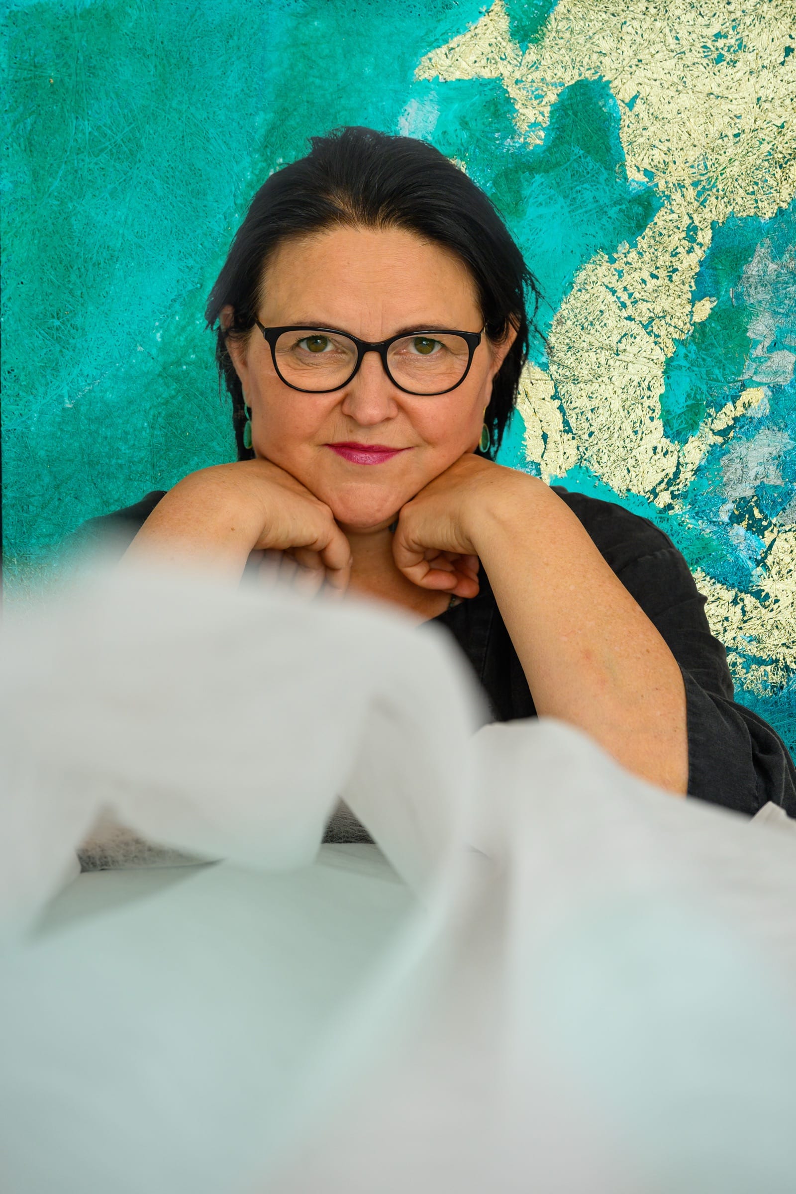 Dorota Roszkowska met haar kin op haar handen, voor een van haar werken in turquoise en bladgoud-slagmetaal.